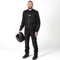 Man met zwarte motorjas met DXR-logo, jeans en helm in de hand.