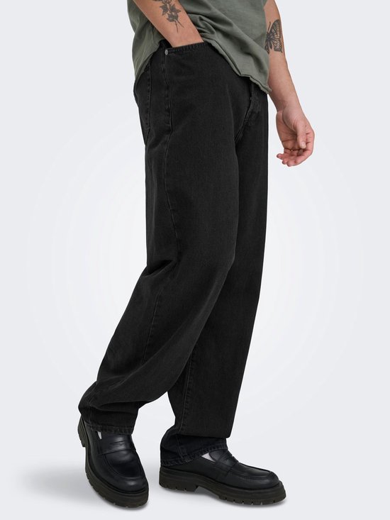 Zijzicht van zwarte jeans met wijde pijpen en zwarte loafers. Mannenmodel met tattoos.