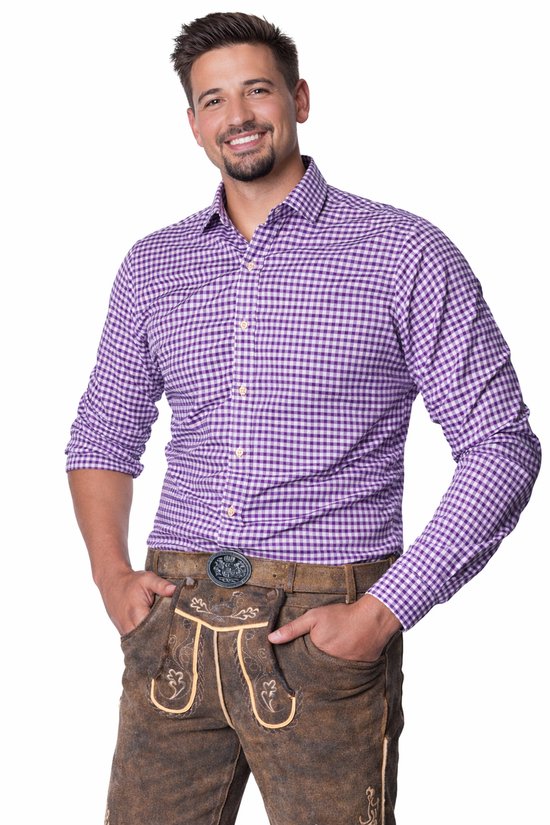 Man met paarse geruite blouse met lange mouwen en bruine lederhosen, handen in zakken.