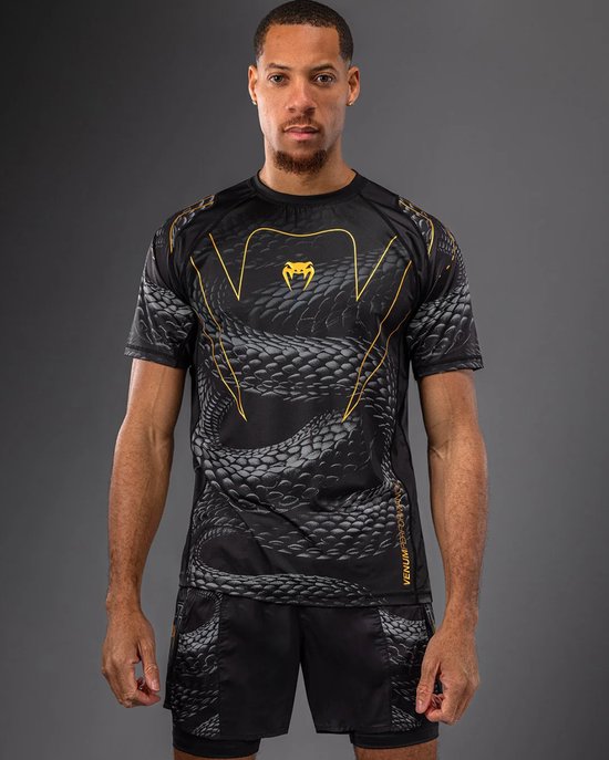 Man met zwart t-shirt met slangenprint en gouden VENUM-logo op de borst. Bijpassende zwarte shorts.