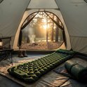 Groene slaapmat in een tent, met kampvuur en bos op achtergrond. Zomerse camping sfeer.