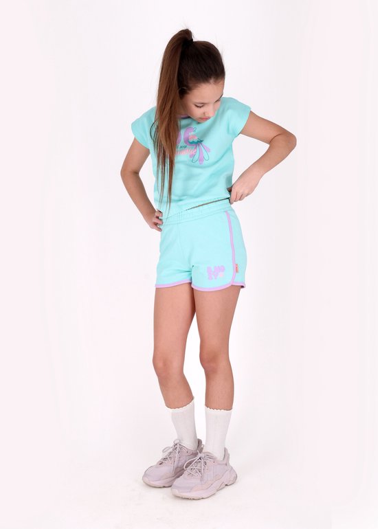 Meisje met paars/lichtblauwe short, mintgroen T-shirt met opdruk, witte sokken en lila sneakers.