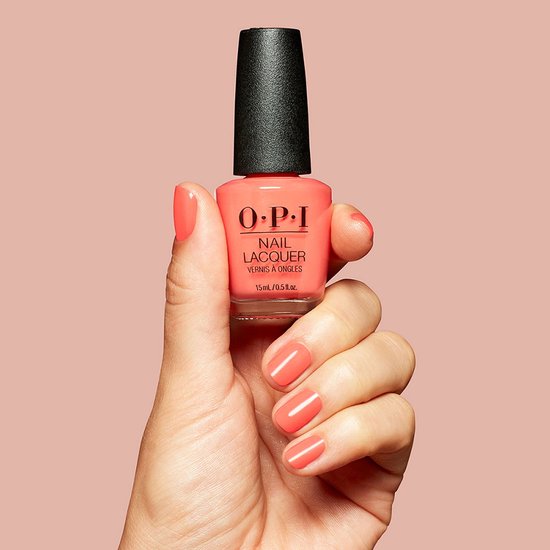 Een hand met een koraalrode O.P.I. nagellak potje, de nagels zijn gelakt.
