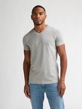 Man draagt een effen lichtgrijs T-shirt met V-hals en een lichtblauwe jeans.