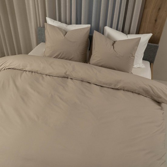 Twee zandkleurige kussens en een bijpassend dekbedovertrek op een bed, met witte lakens eronder.