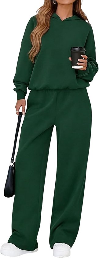 Vrouw houdt koffiebeker vast, draagt donkergroene casual loungewear set met wijde pijpen broek en hoodie.