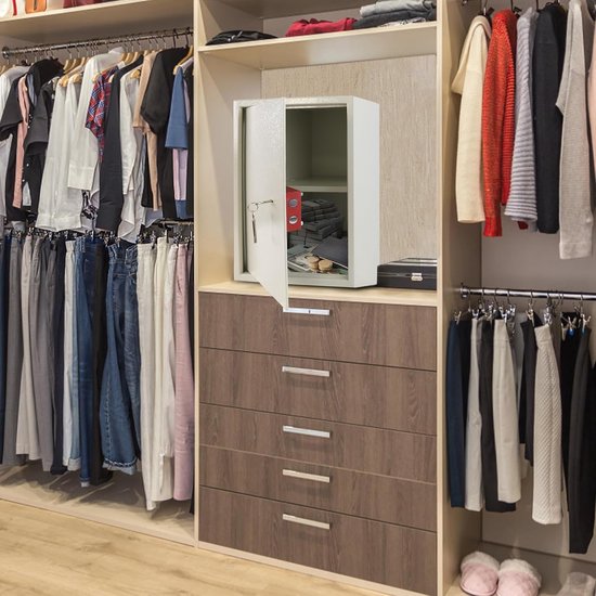 Open crème kluis met geld en sleutels in een inbouwkast vol kleding.