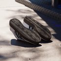 Paar witte Adidas sneakers met zwarte strepen, bruine zolen, op een betonnen ondergrond.