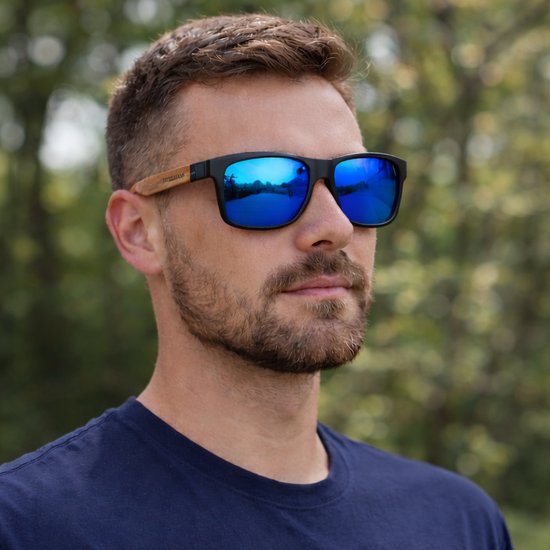 Man met zwarte bril met houten pootjes en blauw spiegelende glazen. De bril reflecteert een waterlandschap.