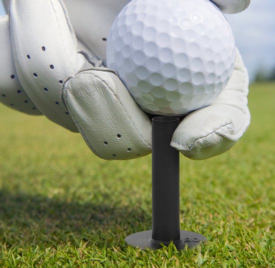 Hand met witte golfhandschoen houdt witte golfbal op zwarte tee met markering 80.