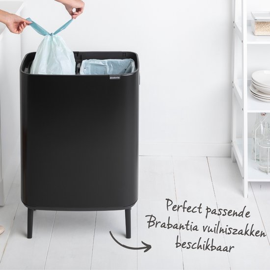 Poubelle Brabantia noire avec deux compartiments ouverts contenant des sacs poubelles bleu clair. Une main ferme un sac par le haut.