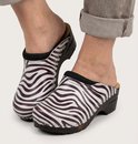 Voeten in zebraprint klompen met zwarte zolen en een grijze broekspijp.