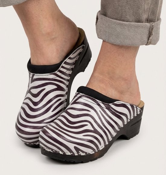Voeten in zebraprint klompen met zwarte zolen en een grijze broekspijp.