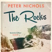 Boekcover met de titel 'The Rocks' van Peter Nichols. Twee mensen omhelzen elkaar op een rotsachtige, zonnige locatie.