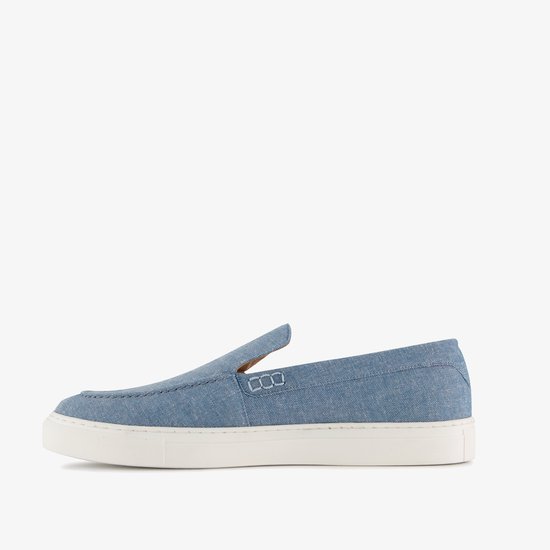 Zijkant van een blauwe denim instapper met witte zool en stiksels.