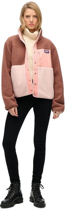 Model draagt bruine, roze en lichtroze fleece jas met spijkerbroek.