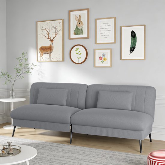 Grijze slaapbank met gestoffeerde rugleuningen en kussens, in een woonkamer met wanddecoratie en meubels.