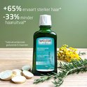 Flesje Weleda haar lotion met rozemarijn, met tekst over sterker haar en minder haaruitval, opgemaakt met takjes rozemarijn en gele bloemen.