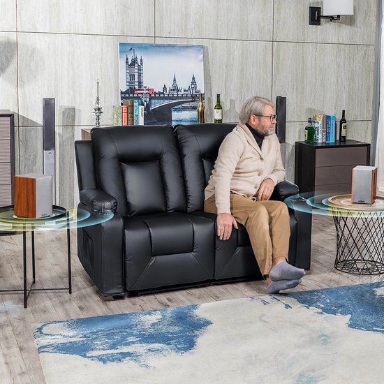 Man met bril zit op zwarte tweezits relaxbank, met bekerhouders en speakers naast zich.
