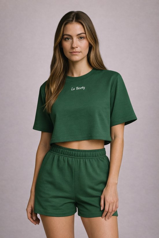 Model in een donkergroene crop top met korte mouwen en 'La Booty' in het wit, met bijpassende shorts met elastische tailleband.