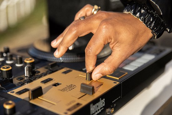 Hand beweegt gouden crossfader op Hercules DJ-controller. DJ-apparatuur in goud en zwart.