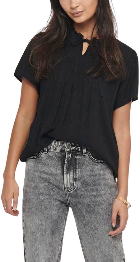 Model met zwarte blouse met korte mouwen, ruchekraag en strikdetail, gecombineerd met een grijze jeans.