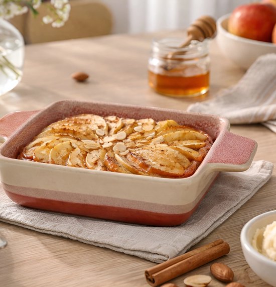 Vierkante ovenschaal met appelcrumble, versierd met amandelen en kaneel.