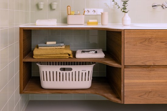 Crème wasmand met ventilatiegaten, gevuld met opgevouwen handdoeken, in een badkamerkast.
