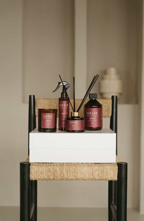 LOULOU Fuerza geschenkset met kaars, roomspray, geurstokjes en wasparfum, gepresenteerd op een houten stoel.