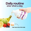 Hand schenkt oranje vloeistof uit fles "Woman Multivitamin" in een doseercupje met fruit op de achtergrond.