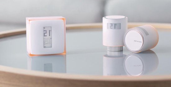 Twee Netatmo slimme thermostaten en een radiatorthermostaat met digitale displays op een glazen tafel.