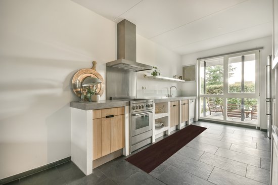 Tapis de cuisine brun foncé à motif bois de feuillus sur sol carrelé gris devant une cuisinière à gaz en acier inoxydable.