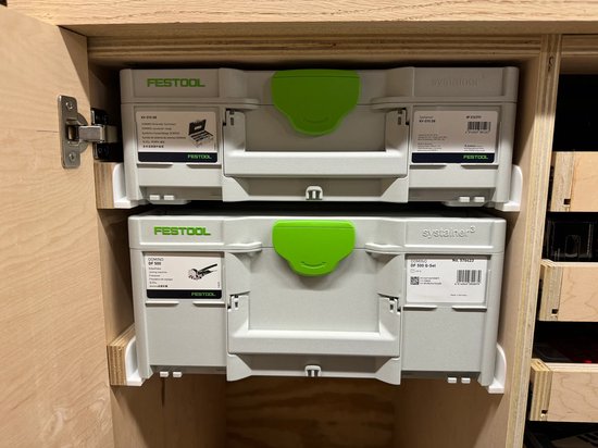 Twee Festool Systainer koffers gestapeld in een houten kast. De bovenste is grijs met groene handgreep en Festool logo. De onderste is grijs met groene handgreep en Festool Domino logo.