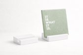 Witte standaard met een groene tegel met de tekst "IT IS WHAT IT IS."