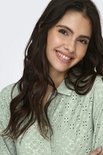 Close-up van een vrouw met golvend bruin haar, lachend, in een lichtgroene blouse met broderie anglaise.