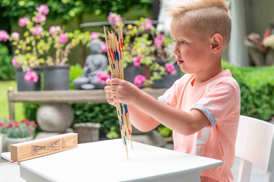 Jongen met blond haar in een oranje shirt, houdt Mikado stokjes vast, speelt buiten.