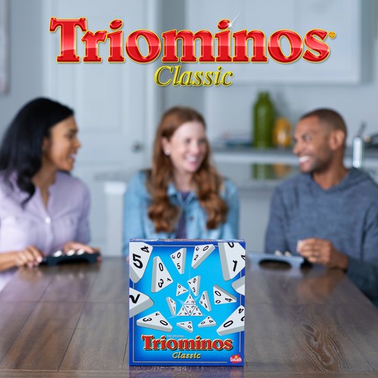Doos van Triominos Classic, het originele strategiespel, met 3 blije spelers op de achtergrond.