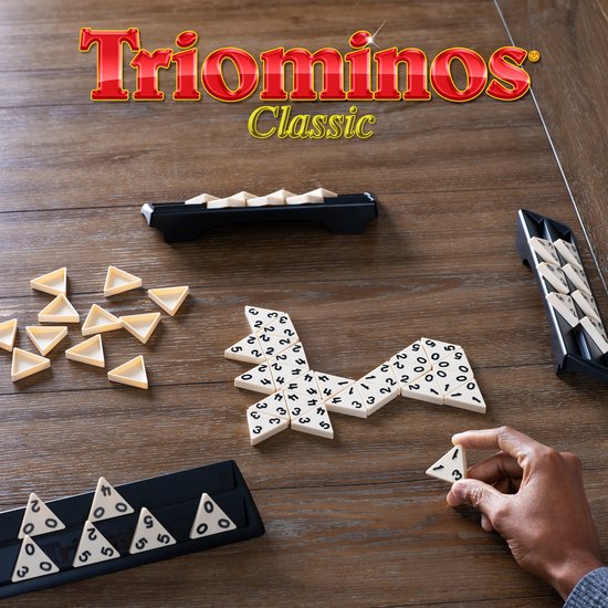 Triominos Classic speelgoed met driehoekige tegels met cijfers op een houten tafel. Een hand legt een tegel.
