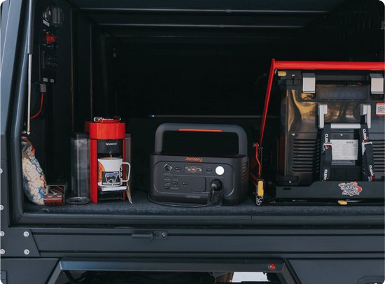 Donkergrijs Jackery Explorer 500 powerstation met oranje accenten, naast een koffiezetapparaat en koelkast in een voertuig.