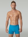 Man met een lichtblauwe Muchachomalo boxershort, logo op de tailleband. Staand voor een grijze achtergrond.