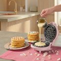 Roze wafelijzer met beslag dat in de vorm wordt gegoten. Op tafel met wafels en confetti.