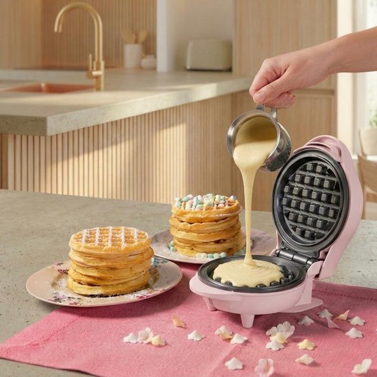 Roze wafelijzer met beslag dat in de vorm wordt gegoten. Op tafel met wafels en confetti.