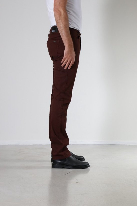 Zijkant van een man in een bordeauxrode broek met een witte t-shirt en zwarte schoenen.