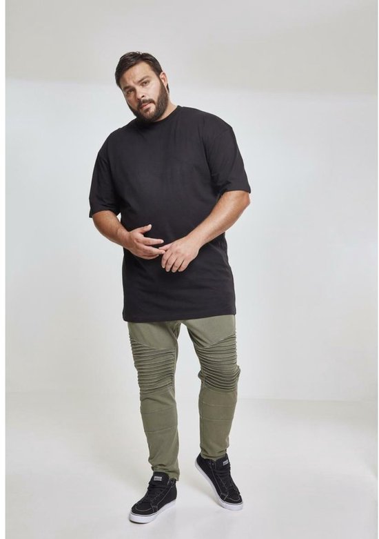 Volle man met baard, draagt een zwart T-shirt en olijfgroene broek.