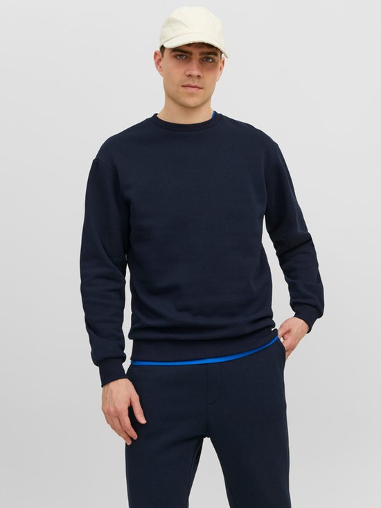 Man met lichtblauwe pet draagt een donkerblauwe trui en trainingsbroek met blauwe tailleband.