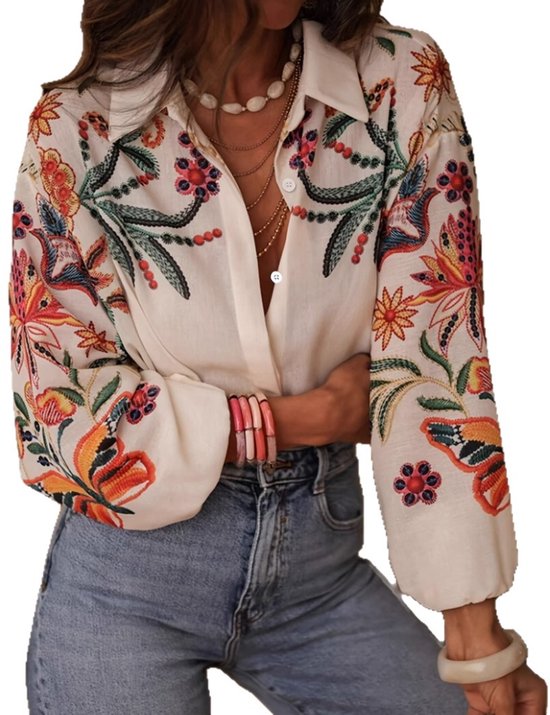 Chemise couleur crème à manches longues, ornée de broderies florales et de papillons colorés. Le modèle porte un jean.
