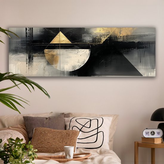 Abstract schilderij met geometrische vormen in zwart, wit en goud, hangend boven een bed.