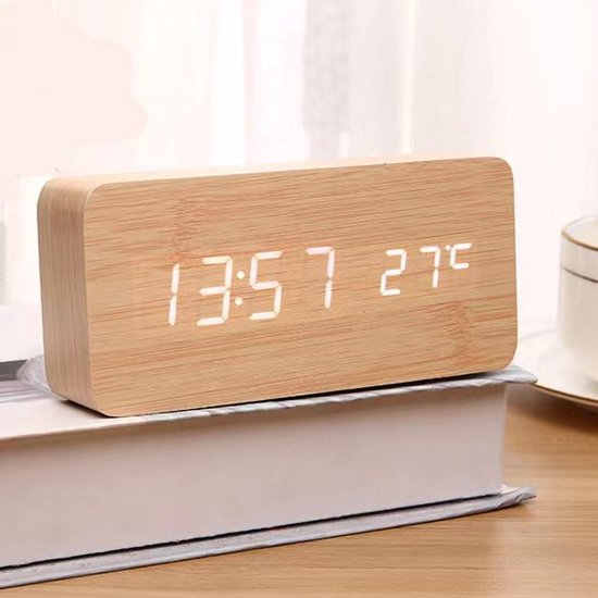 Houten digitale klok met witte LED-tijdweergave (13:57) en temperatuur (27°C), geplaatst op een boek.