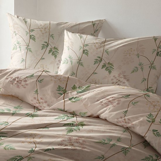 Twee beige kussenslopen met een groene en bruine bloemenprint, naast een opgemaakt bed met hetzelfde dekbedovertrek.
