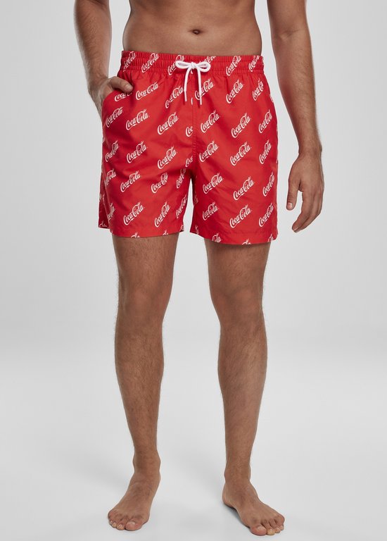 Man die rode zwemshorts draagt met een all-over wit Coca-Cola logo patroon.